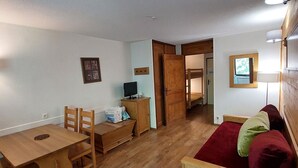 A compact room with a wooden table, a single chair, a bunk bed, and a red sofa. - Cozy studio with west balcony, WIFI, covered parking (Brides-les-Bains)