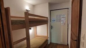 A small, narrow room with a bunk bed, a door with a notice board, and a light fixture on the ceiling. - Cozy studio with west balcony, WIFI, covered parking (Brides-les-Bains)