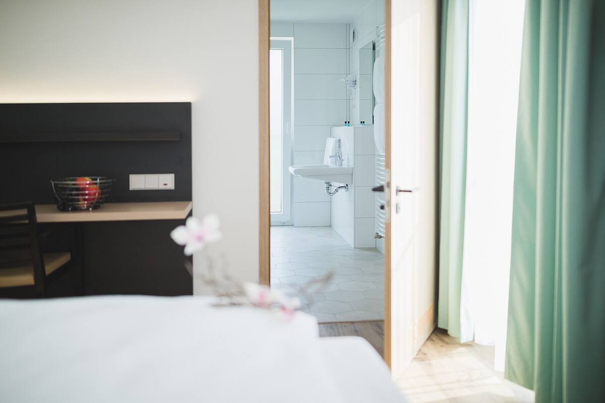 A hotel room with a bed, a desk with a basket, and a view into the bathroom.