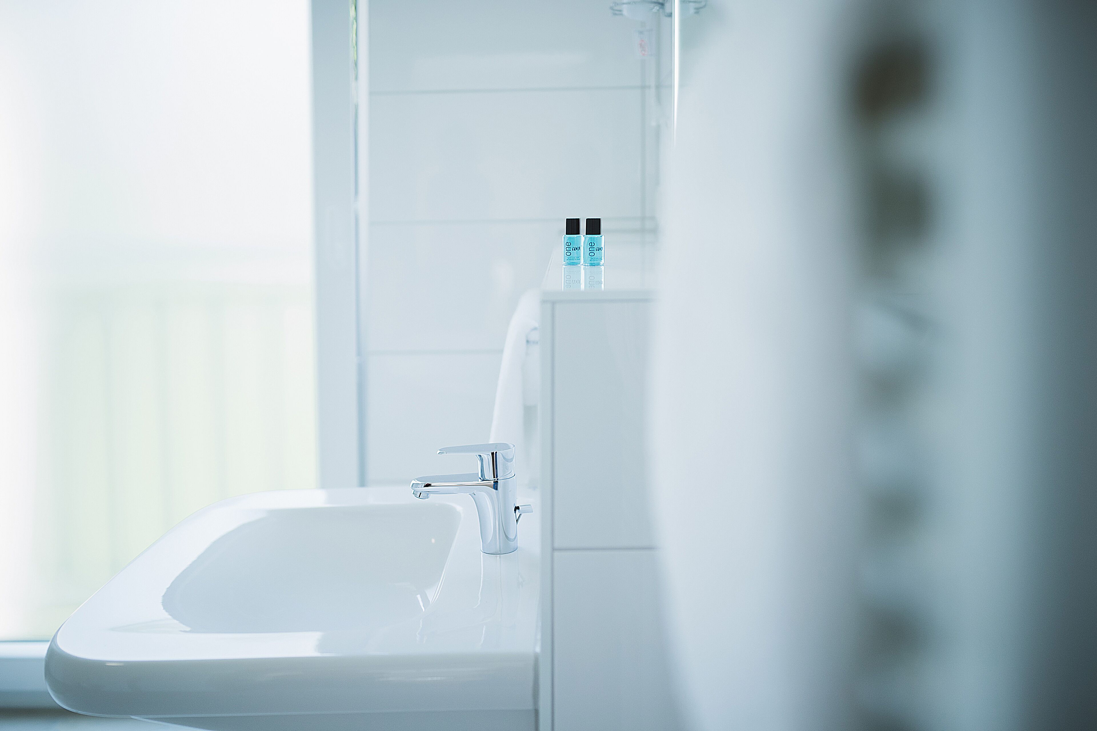 A modern bathroom with a white sink and a chrome faucet. There are two bottles of hand soap on the sink.