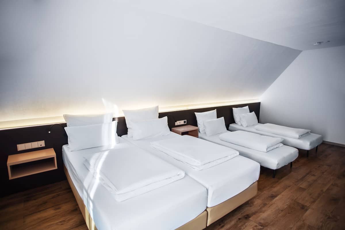 A modern hotel room with a sloped ceiling, a wooden floor, and a large bed with white linens.