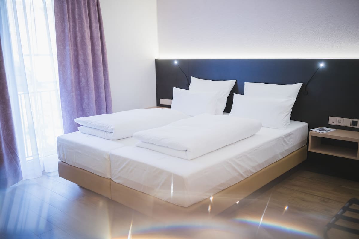 A modern hotel room with a large bed, a nightstand, and a window with curtains.