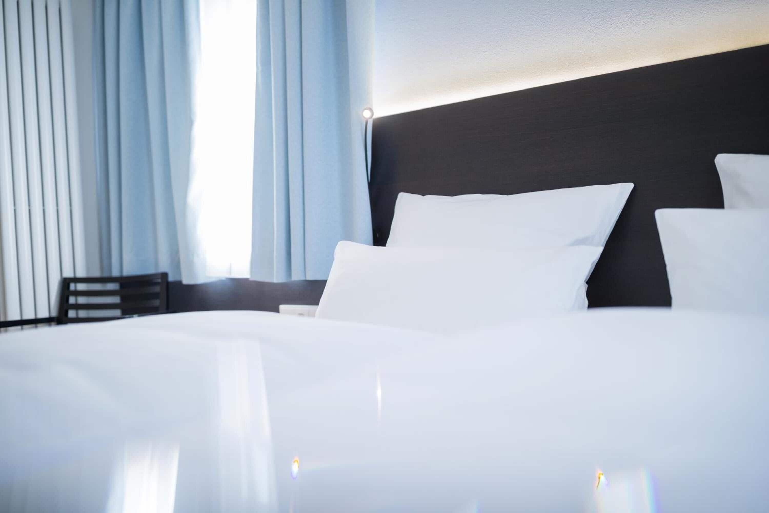 A neatly made bed with white linens in a hotel room.