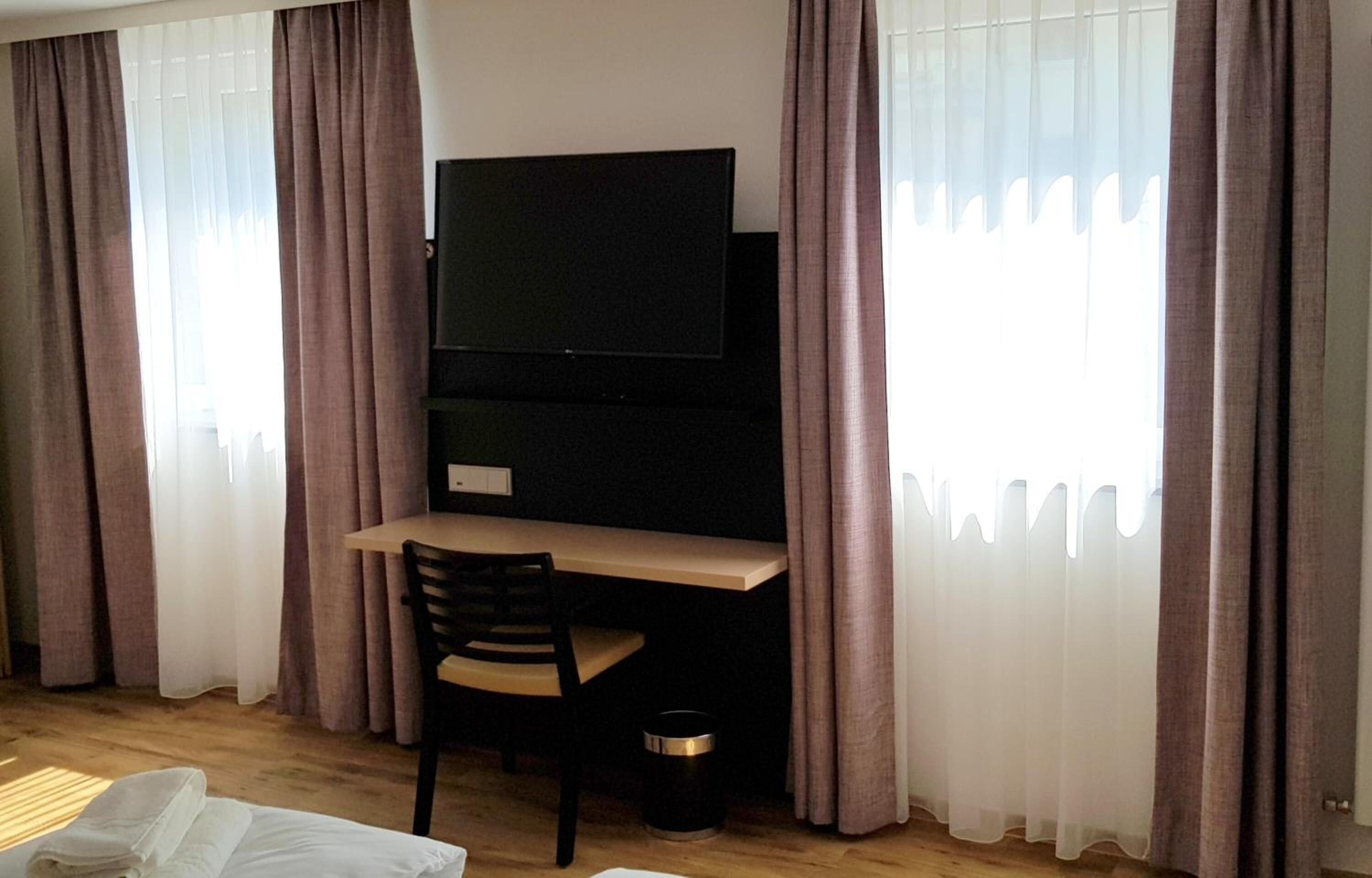 Ein Hotelzimmer mit Bett, Schreibtisch mit Stuhl, Fernseher und Vorhängen.