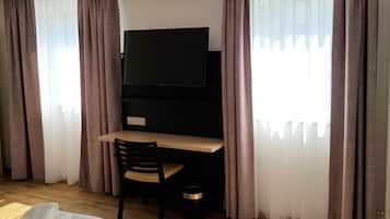 Ein Hotelzimmer mit Bett, Schreibtisch mit Stuhl, Fernseher und Vorhängen.