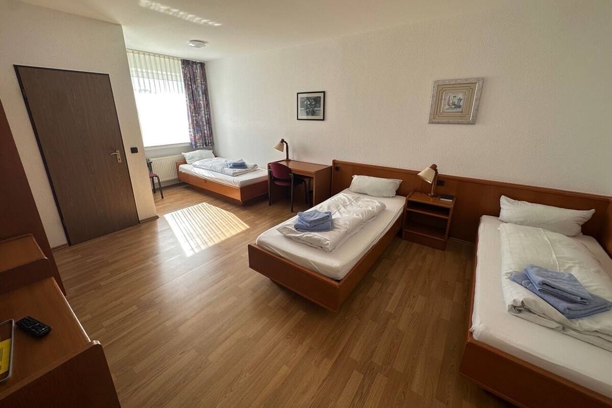 A hotel room with three single beds, a desk, a chair, and a small table.