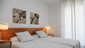 A double bed with two pillows, a wooden headboard, a bedside table with a lamp, and two wall-mounted paintings of flowers.