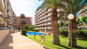 A hotel corridor with a pool, palm trees, and a clear sky.