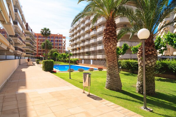 A hotel corridor with a pool, palm trees, and a clear sky.