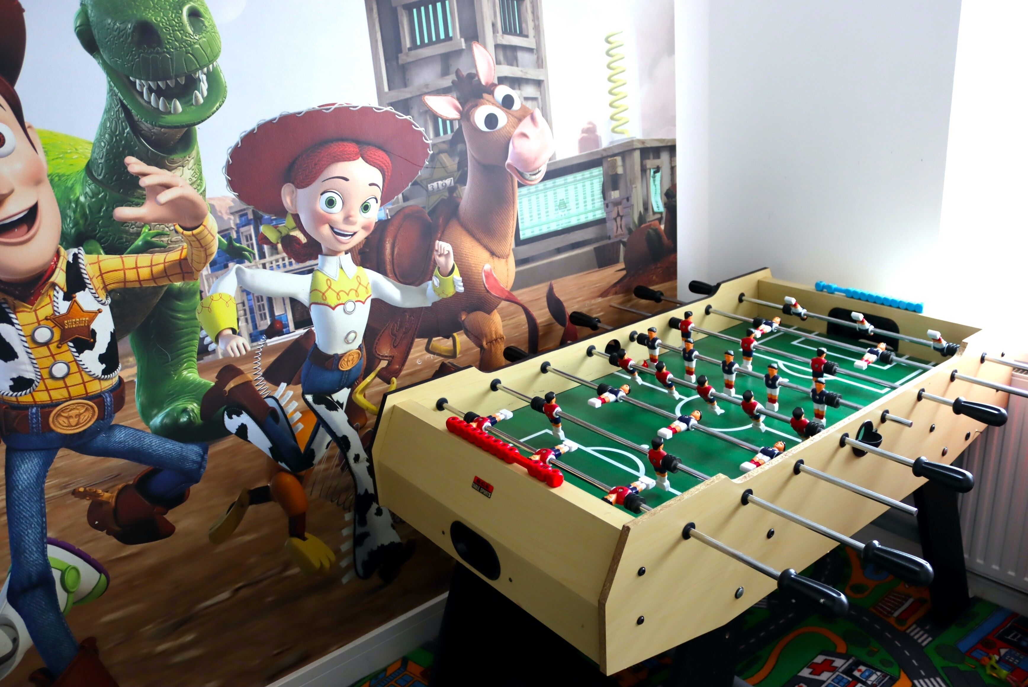 Een tafelvoetbaltafel met speelfiguurtjes in een kamer met een muurschildering van stripfiguren.