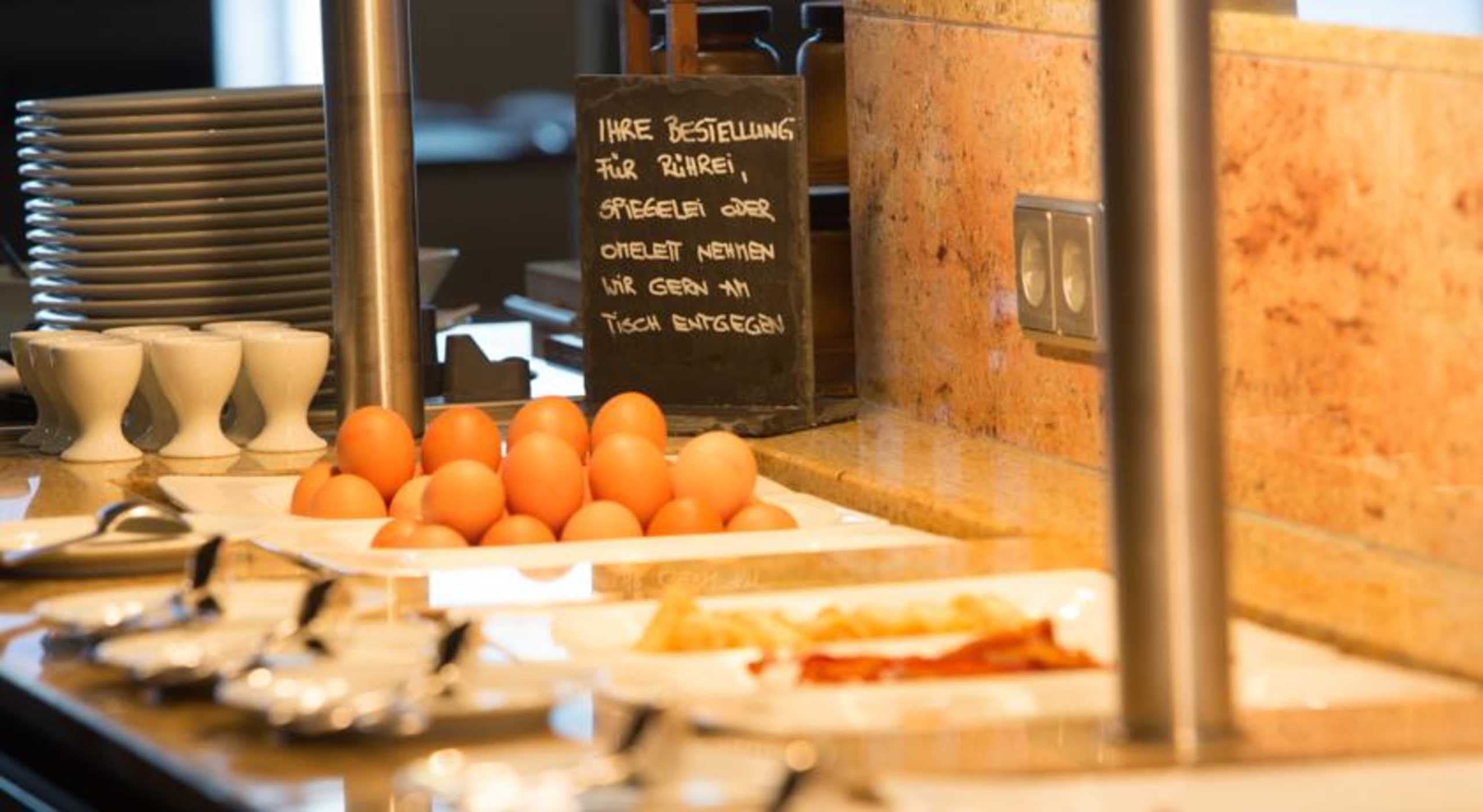 A breakfast buffet with eggs, bread, and a sign in German.