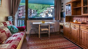 A cozy room with a sofa, a dining table with chairs, a window with a view of a village, and wooden cabinets. - Cozy studio for 4, near Val d'Isère center, with WIFI (Val-d'Isère)