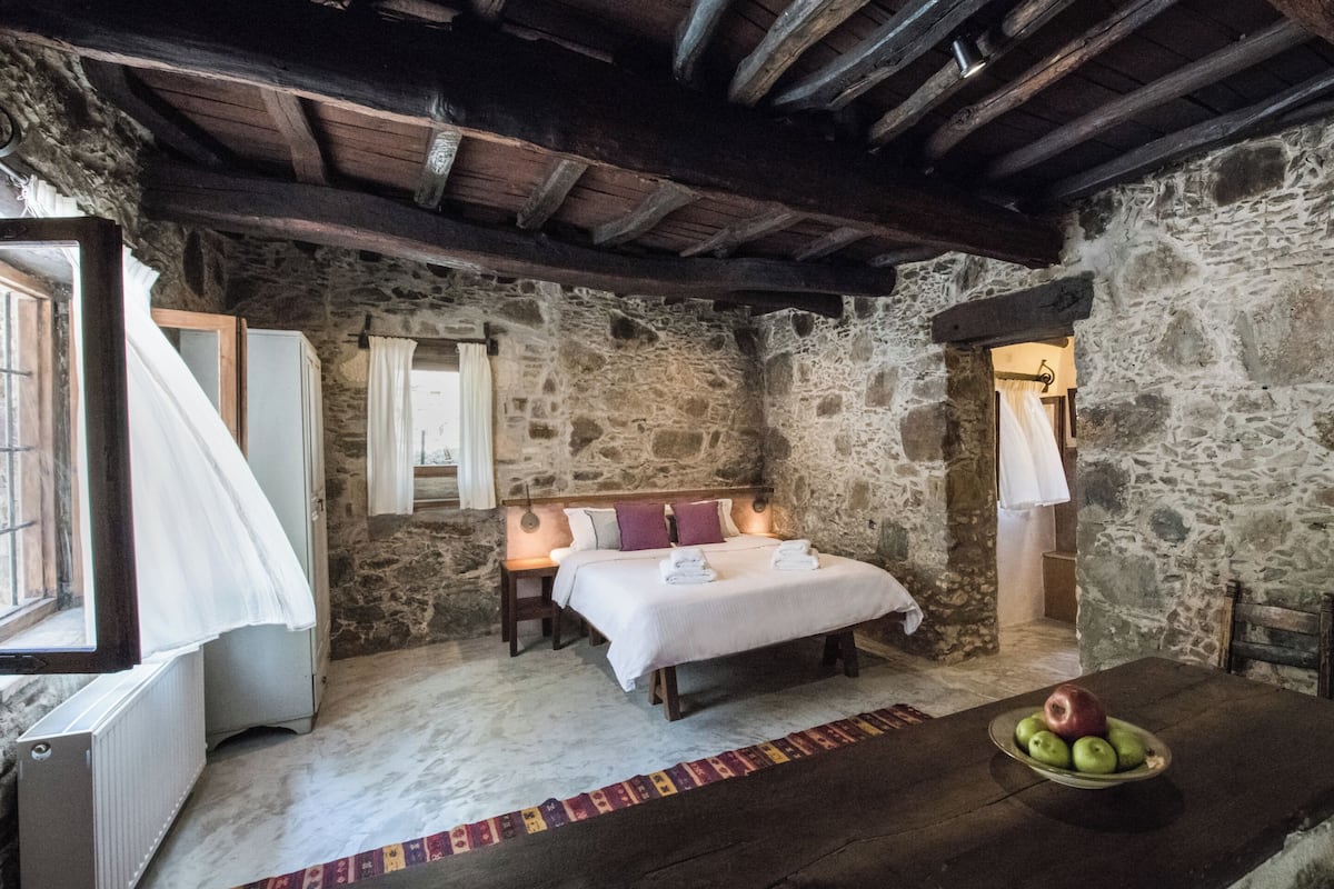 A stone-walled bedroom with a bed, bedside tables, and a fruit bowl.