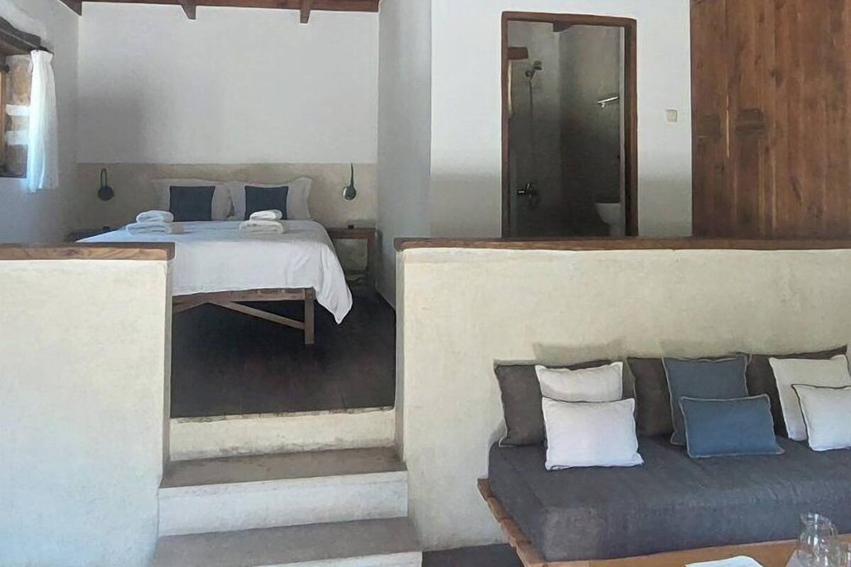A room with a bed, a sofa, a wooden table, and a red patterned rug.