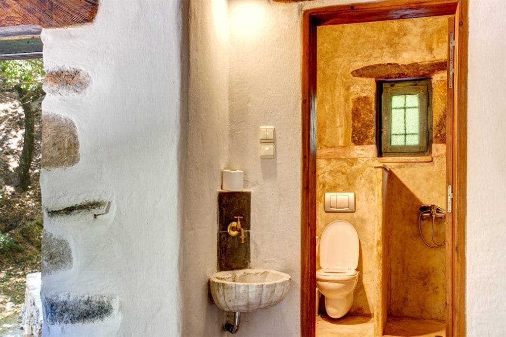 A rustic bathroom with a stone sink, a wooden door, and a small window.