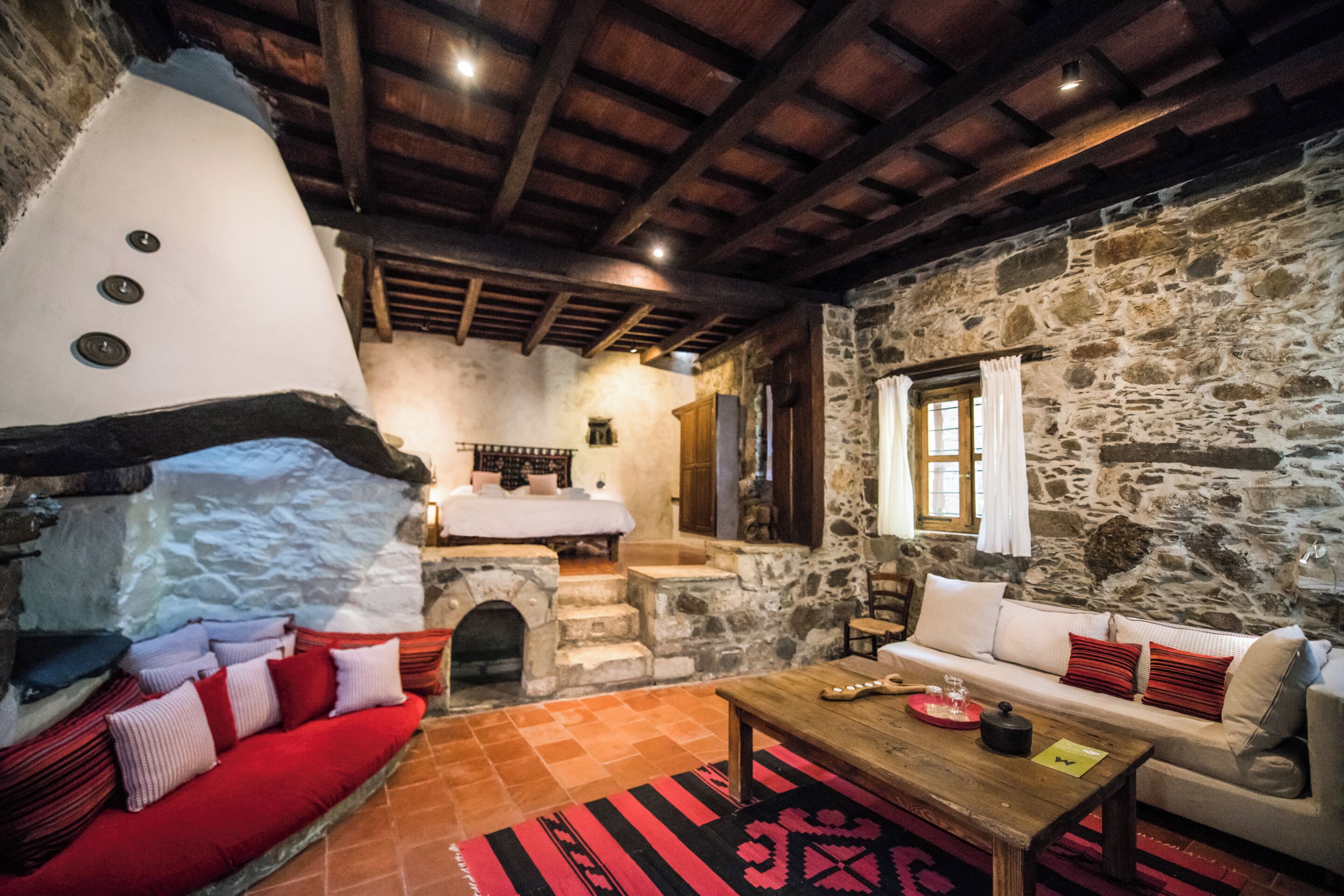 A rustic stone interior with a stone fireplace, wooden beams, a sofa, and a coffee table.