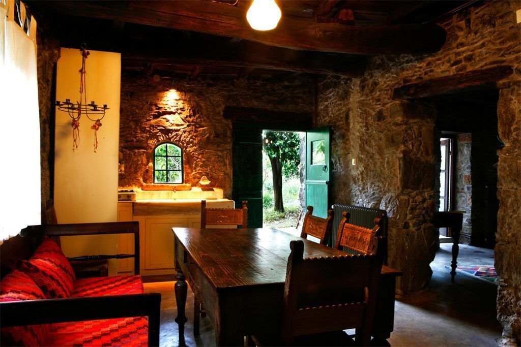A rustic interior with a stone wall, wooden furniture, and a window with a view of greenery.