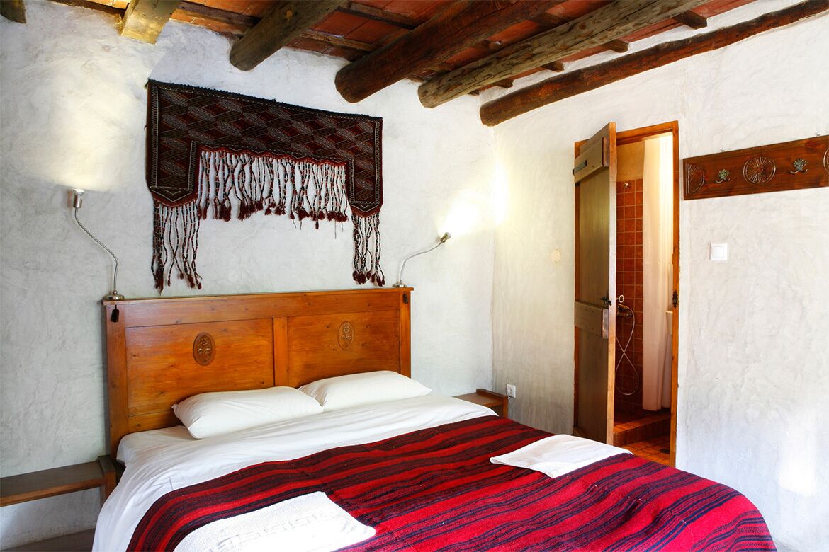 Un lit avec une tête de lit en bois, une couverture à rayures rouges et noires, et un élément décoratif suspendu.