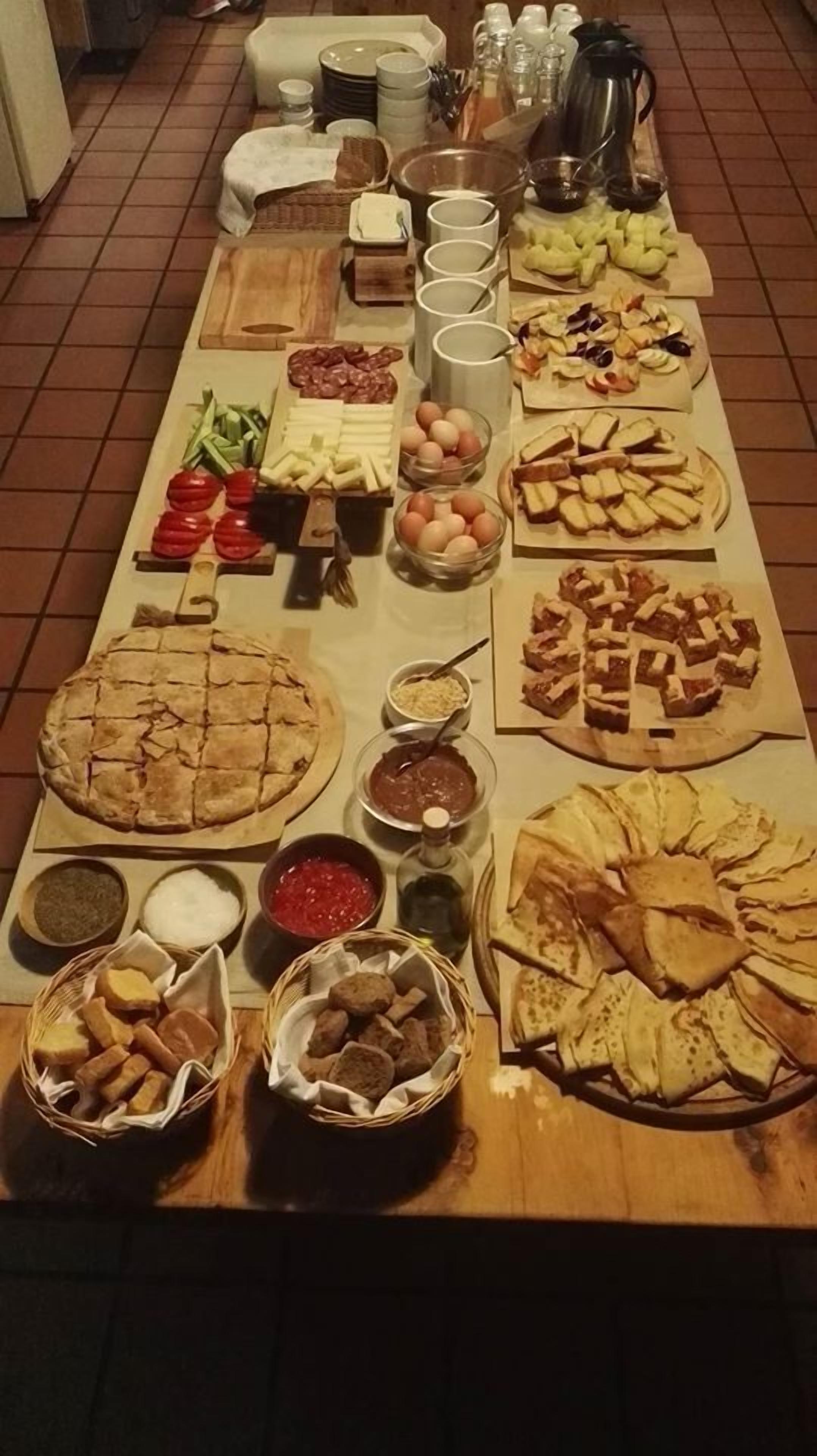 Uma mesa com diversos alimentos e acompanhamentos, incluindo uma torta grande, tigelas de frutas e vários tipos de pão.