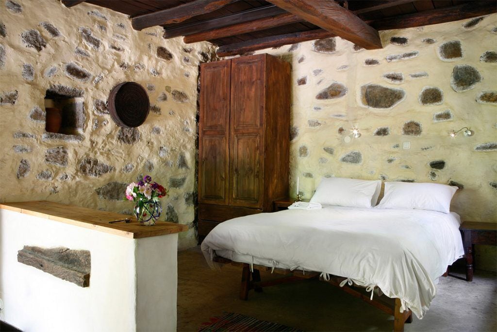 Une chambre rustique avec un mur en pierre, un lit en bois et une armoire en bois.