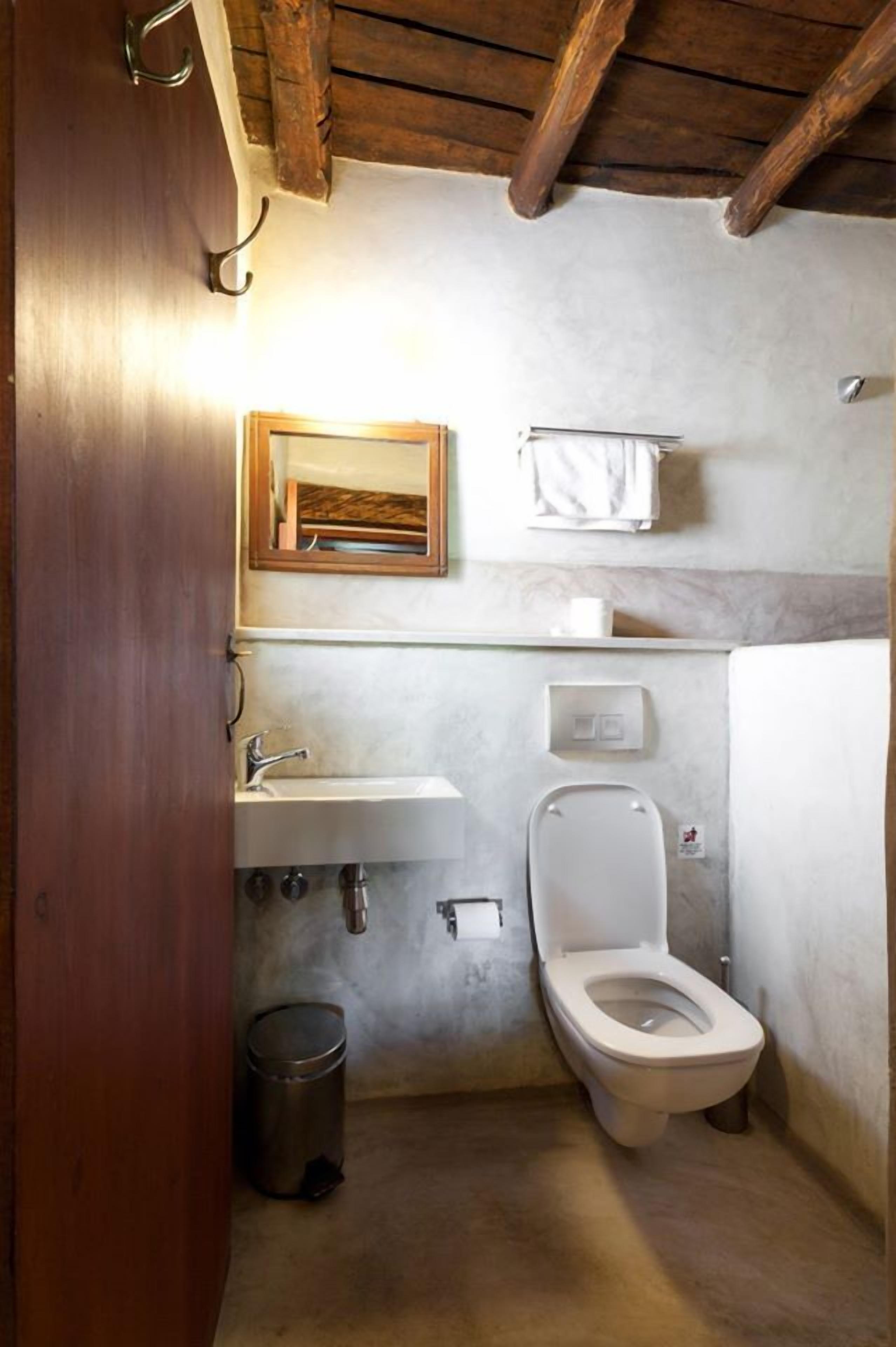 A small, compact bathroom with a wooden ceiling, a sink, a toilet, and a trash can.