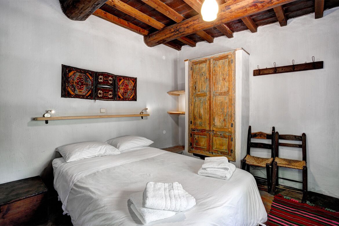 A bedroom with a bed, wooden wardrobe, and a wall-mounted shelf.