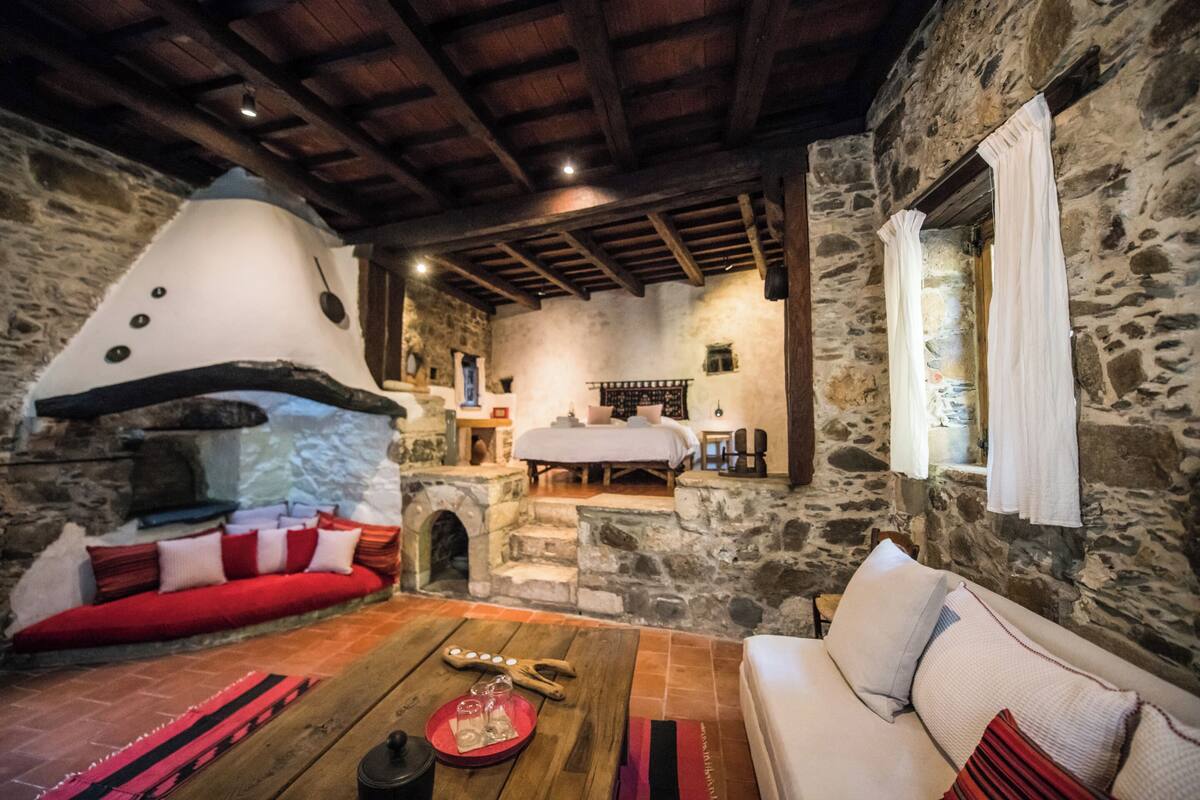 A cozy room with a stone wall, a wooden ceiling, a bed, and a red sofa.