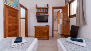 Ein Zimmer mit zwei Betten, einem Holzschrank, einem Fernseher und einem Bücherregal.