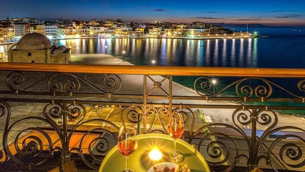 Eine Terrasse mit Tisch für zwei Personen, mit Blick auf eine städtische Skyline am Wasser bei Dämmerung.