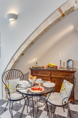 A dining area with a round glass table, black metal chairs, and a wooden cabinet with a fruit bowl and candles.