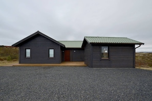 A two-story cabin with a gravel driveway, a wooden door, and a small attached shed. - Odinsve Country Home (Selfoss)