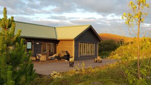A cabin with a covered deck, outdoor seating, and a view of the surrounding landscape. - Odinsve Country Home (Selfoss)