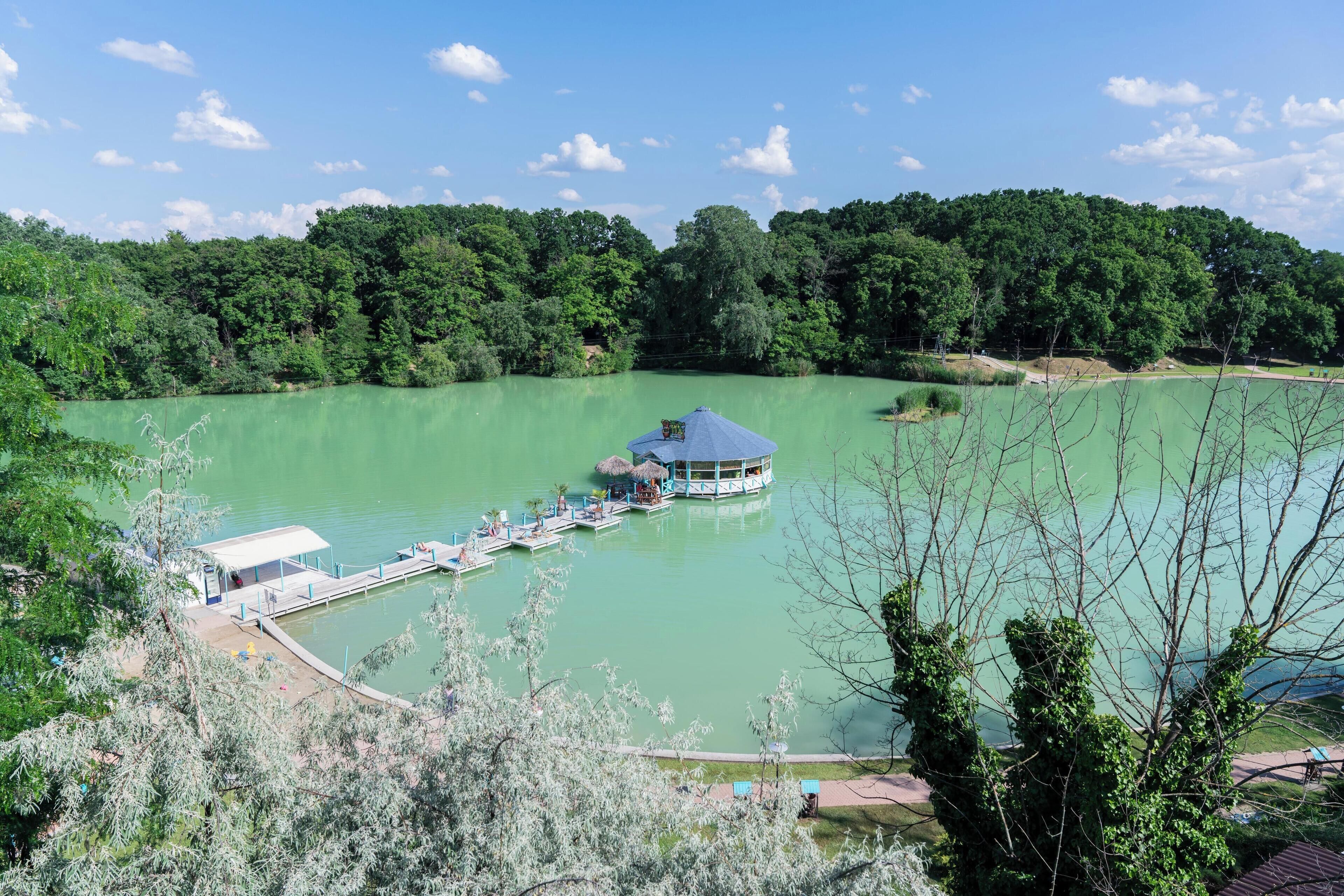 A lakeside hotel with a dock extending into the water, surrounded by lush greenery.