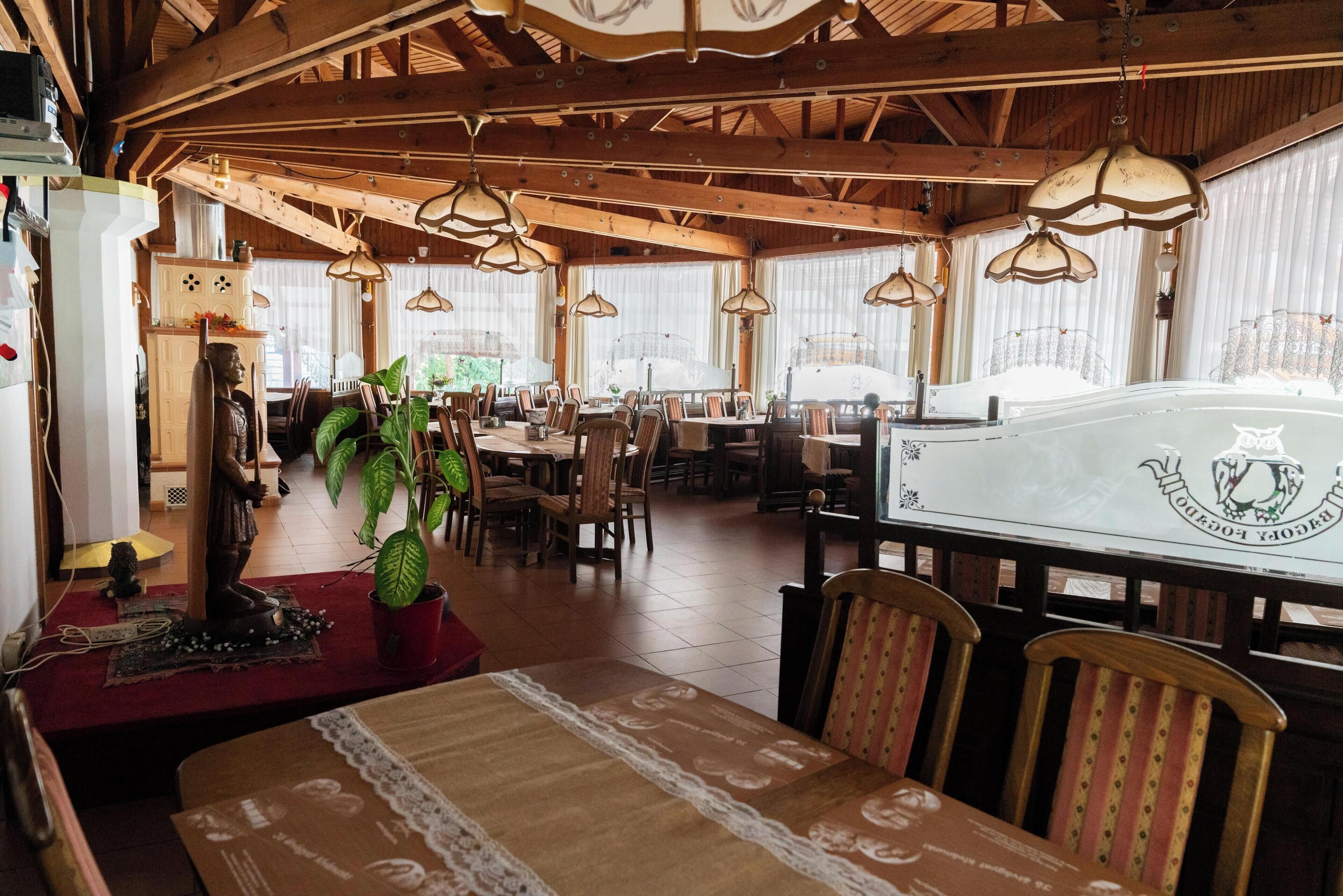A spacious restaurant with wooden beams, hanging lamps, and a large table with a decorative table runner.