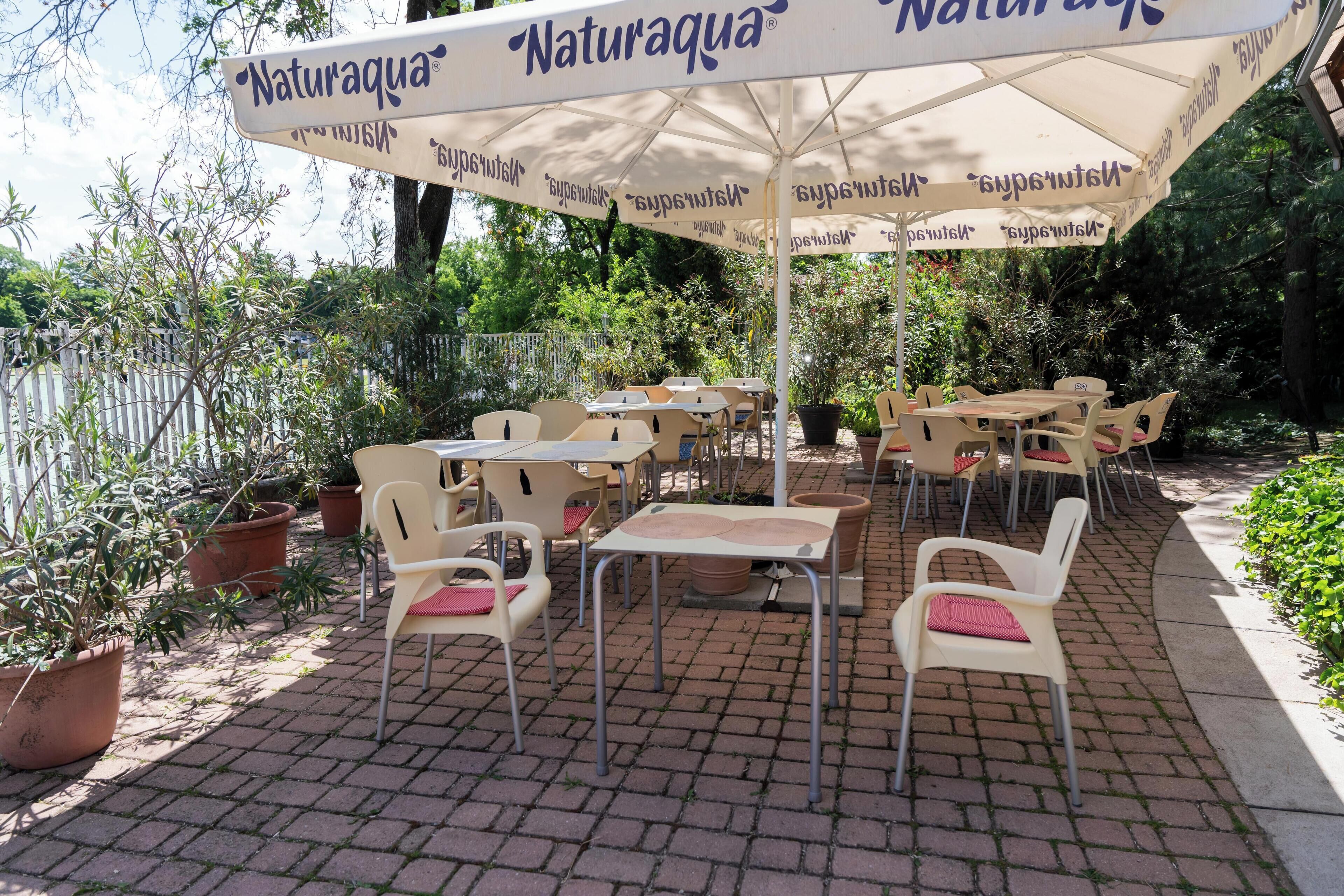 Un patio al aire libre con mesas y sillas bajo un gran paraguas con la marca 'Naturaqua'.