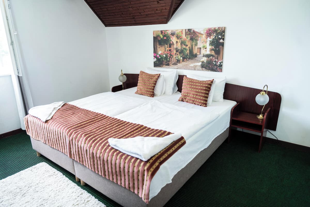 A neatly made bed with striped bedding, a bedside table with a lamp, and a wall-mounted picture of a street scene.