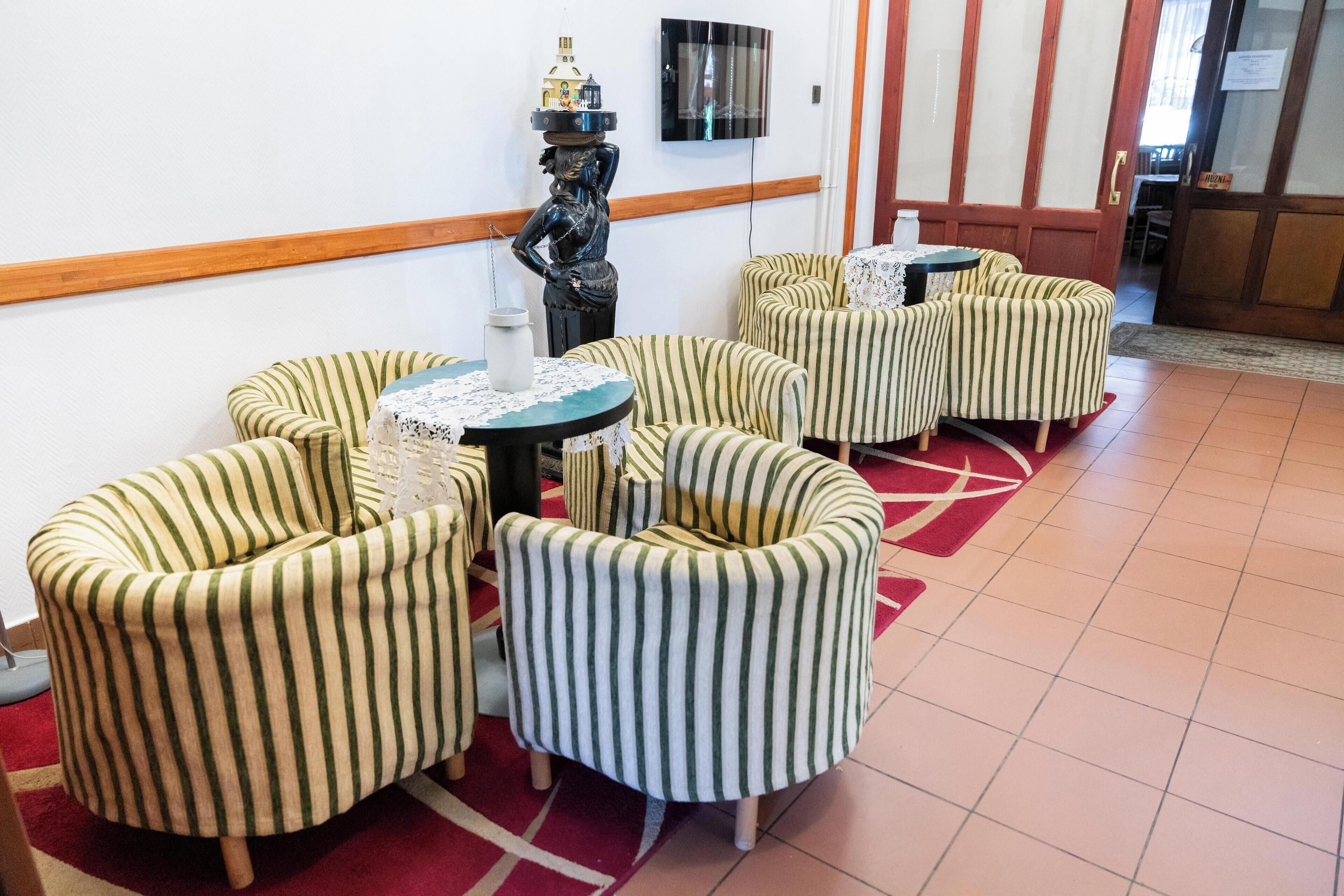 Una habitación con sillones a rayas, una pequeña mesa redonda, una estatua decorativa y un televisor de pantalla plana montado en la pared.