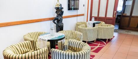 Una habitación con sillones a rayas, una pequeña mesa redonda, una estatua decorativa y un televisor de pantalla plana montado en la pared.