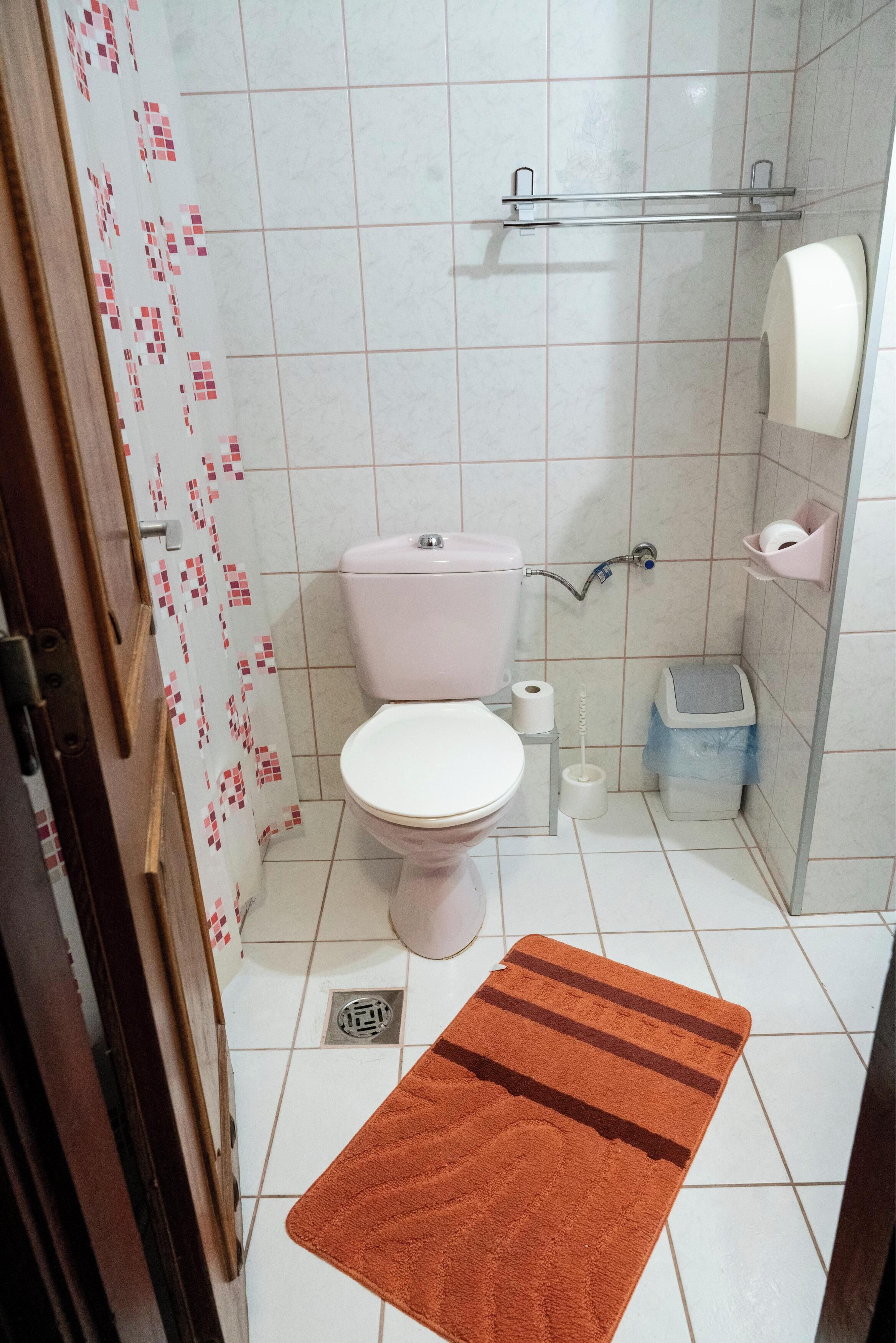 Un baño con inodoro, ducha, secador de manos y cubo de basura.