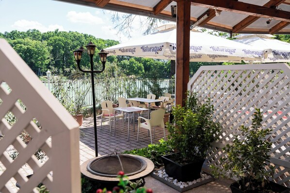 An outdoor patio with tables and chairs, surrounded by potted plants and a white lattice fence. - Bagoly Fogadó (Gyomro)