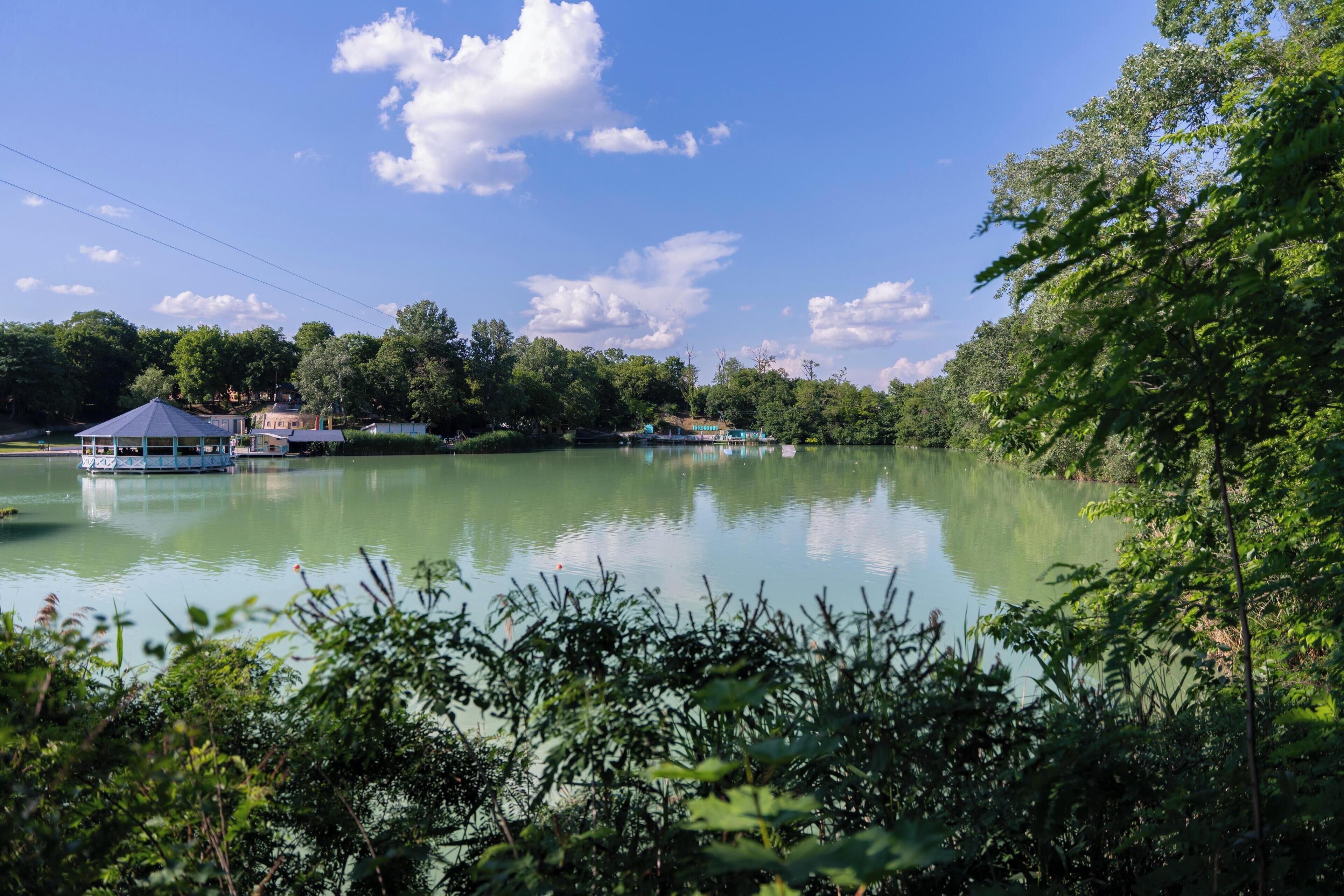 A calm lake with a gazebo and a small building on the shore.
