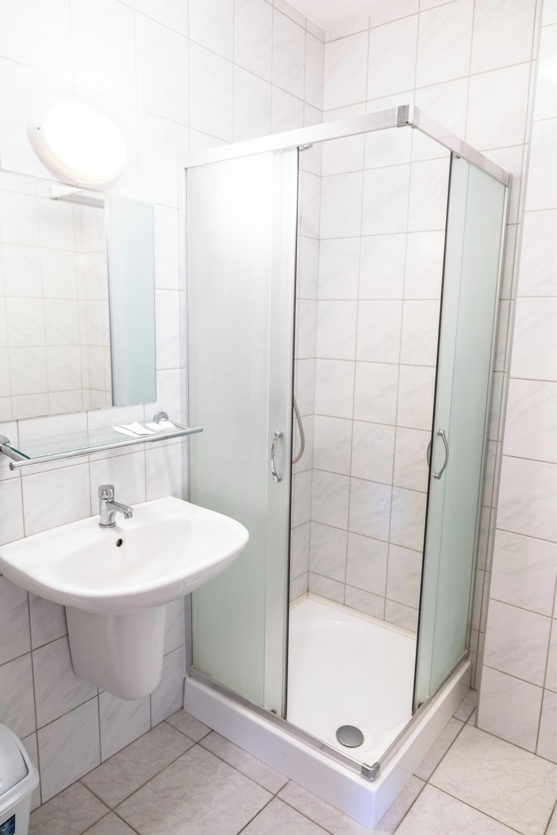 Un baño con ducha compartimentada por vidrio, un lavamanos blanco y un espejo sobre él.