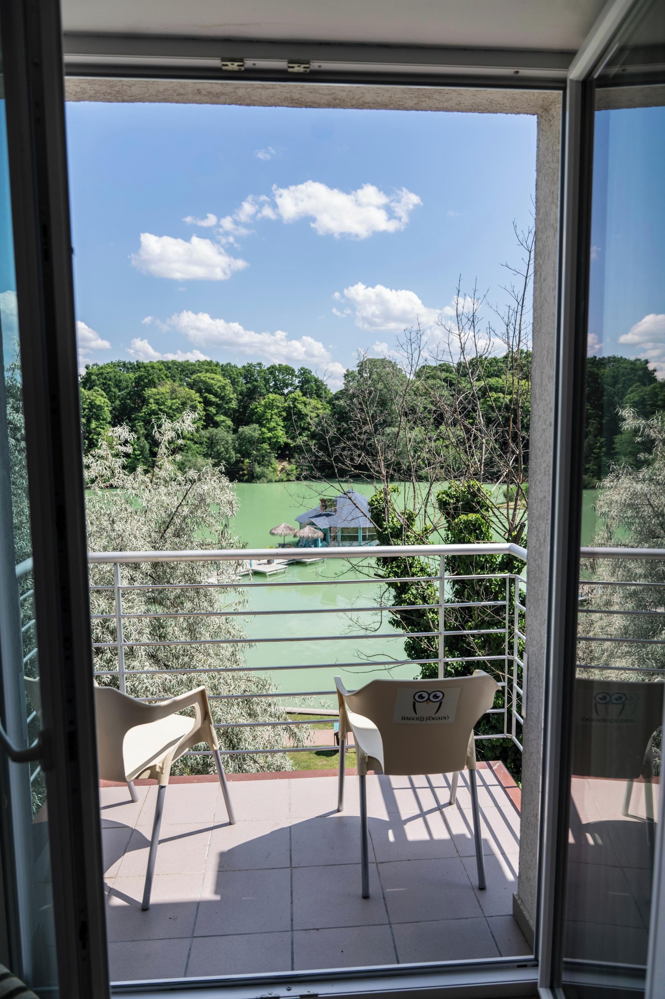 Un balcón con dos sillas, vista a un área verde con árboles y un edificio pequeño.