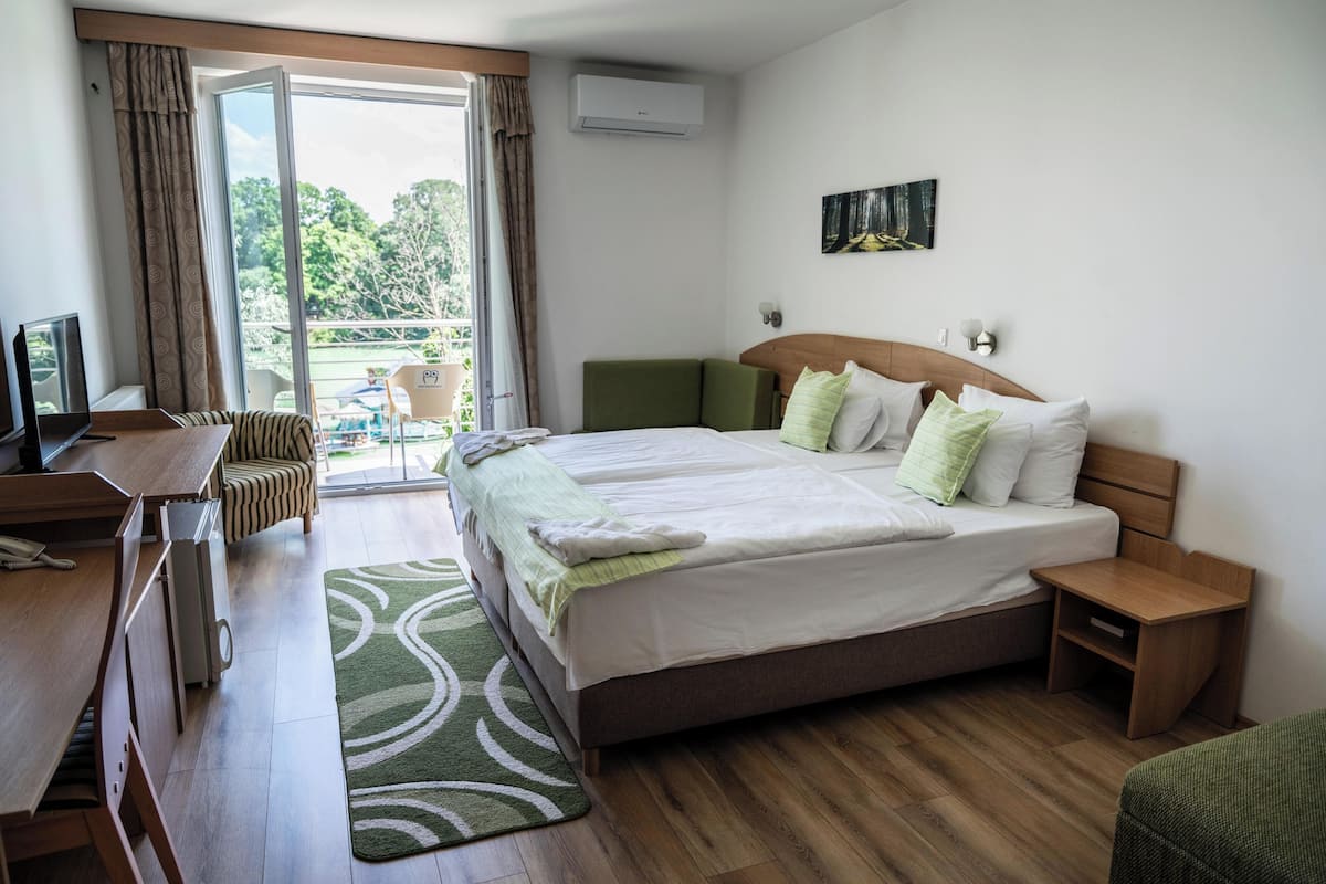 A hotel room with a bed, a desk, a chair, a small table, and a view of the outdoors.