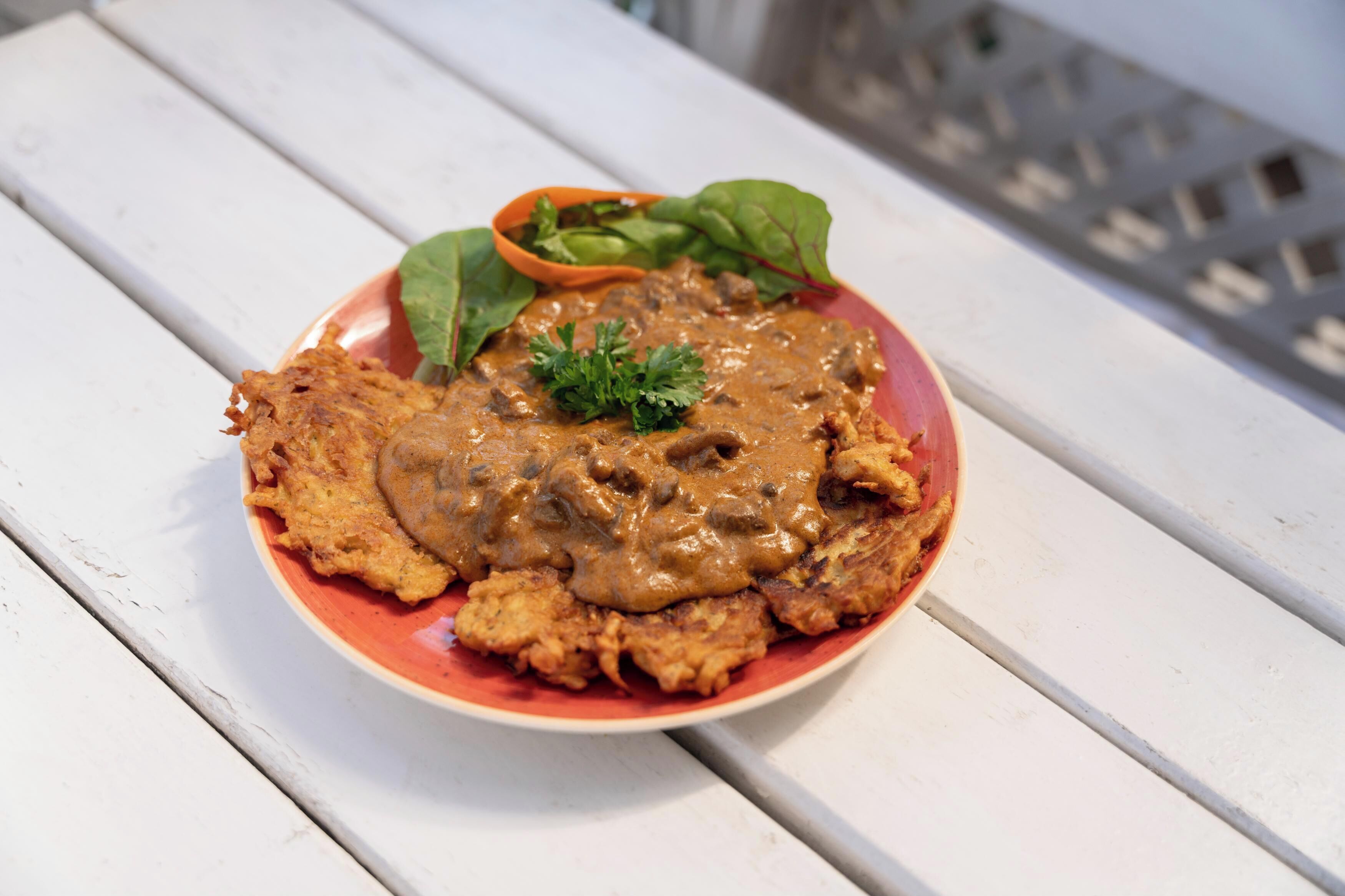 A plate of food with a creamy sauce and greens on a white wooden table.