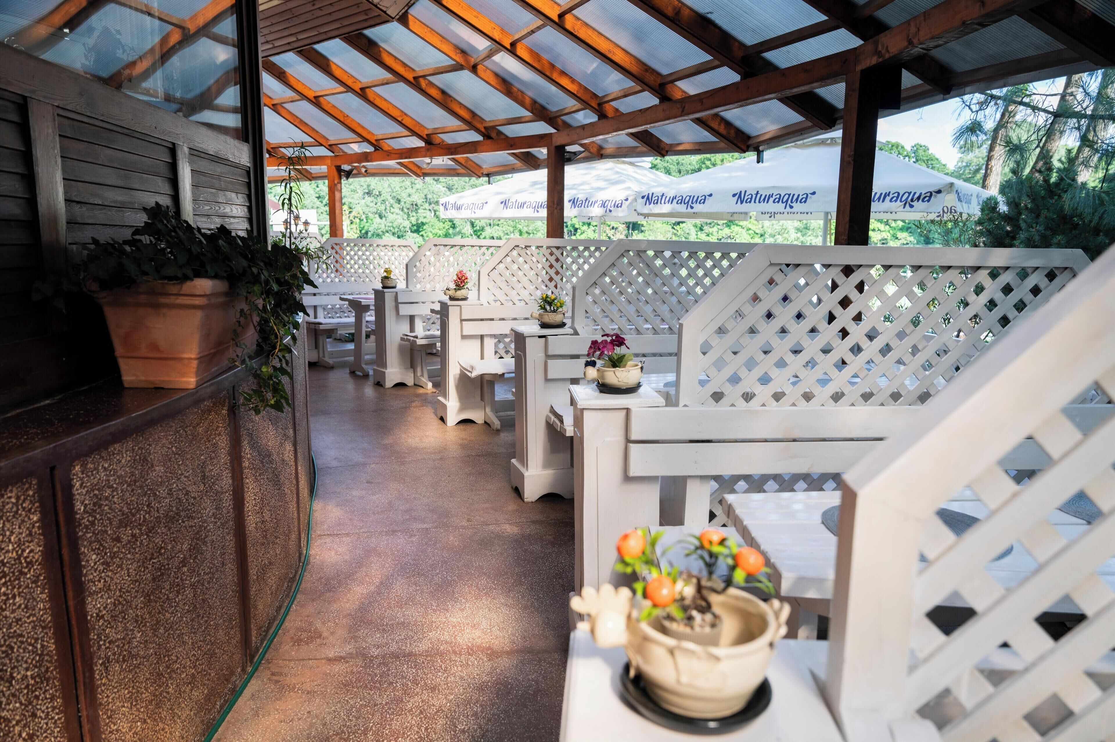 A covered outdoor seating area with white lattice furniture, potted plants, and umbrellas branded "Naturaqua".