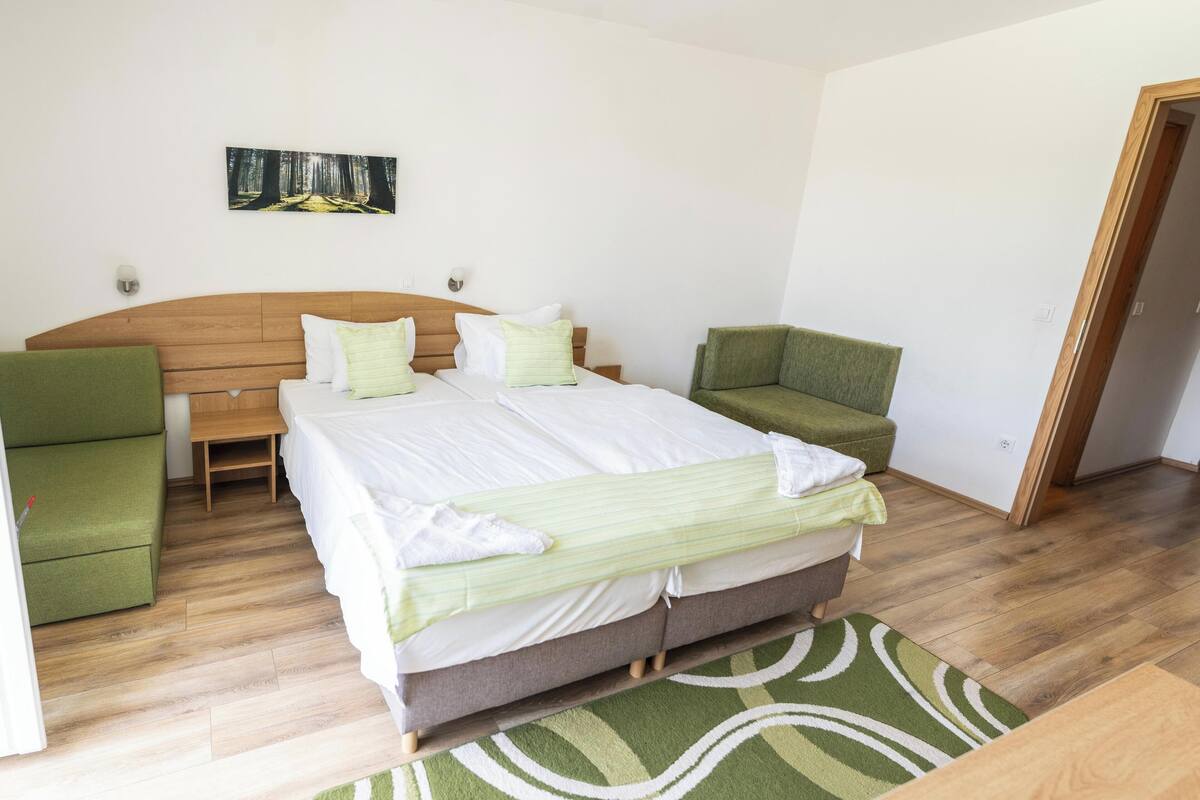 A bedroom with a wooden headboard, a large bed with white linens, two green armchairs, and a green patterned rug.