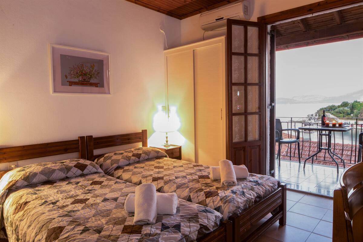 A hotel room with two beds, a painting on the wall, a lamp, and a balcony with a table and chairs.