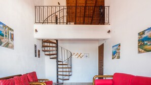 A spacious room with a wooden ceiling, a staircase leading to a balcony, and two red sofas. - Villa Perris Studios (Corfu)
