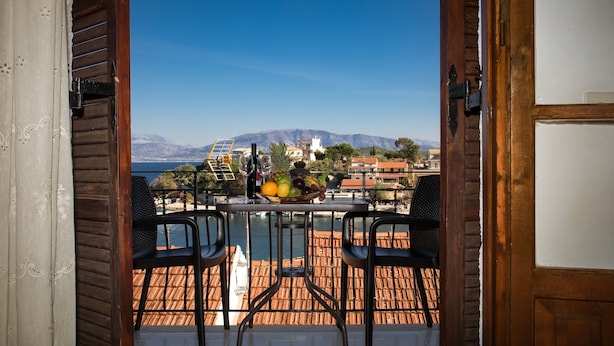 A balcony with a table set for two, overlooking a body of water and a mountainous landscape. - Villa Perris Studios (Corfu)